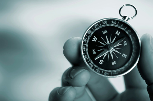 A close up blue tinted image of a male caucasian hand holding a generic compass. Shot with a shallow depth of field with blurred background with copyspace. 