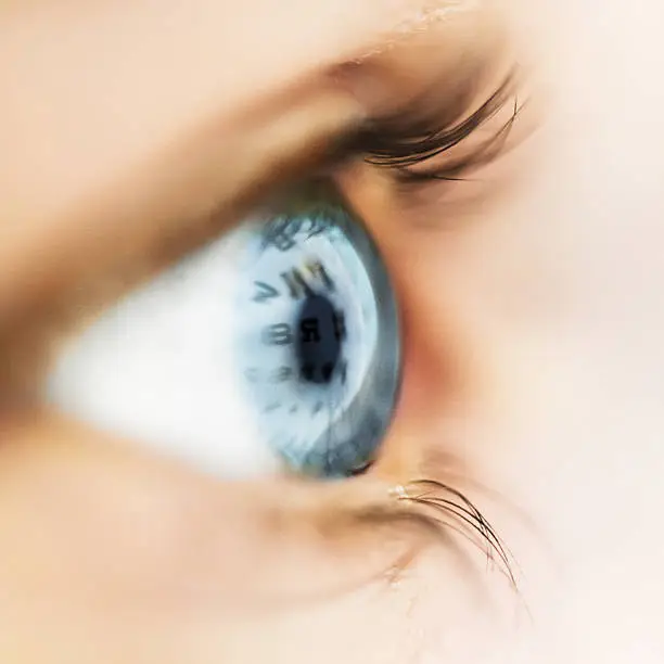 Macro shot of a womans eyeball reflecting an eye test chart.