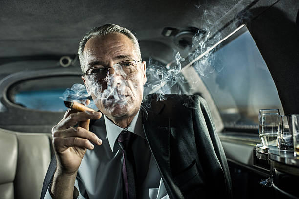 Mature adult businessman smoking a cigar in limousine. Successful businessman sitting in a limousine and smoking a Cuban cigar. He is looking at the camera. man cigar stock pictures, royalty-free photos & images
