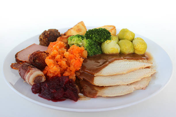 Photo showing a traditional British Christmas dinner with 'all the trimmings' and plenty of gravy.  These include slices of roast turkey, roast potatoes, carrot and swede mashed together, broccoli, stuffing, a chipolata sausage with bacon, and a spoonful of cranberry sauce.