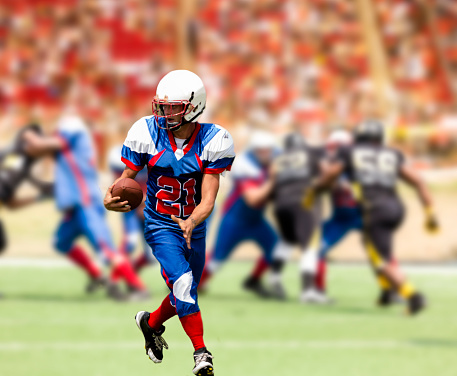 Sports emotions. American football in a large open stadium. Young agile american football player running fast towards goal line. Touchdown. Fans