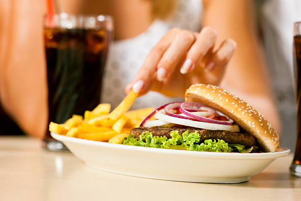 dos mujeres comiendo hamburguesas y bebidas gaseosas - white food and drink industry hamburger cheeseburger fotografías e imágenes de stock