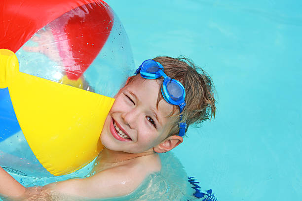 heureux petit garçon avec ballon de plage coloré dans la piscine - beach ball swimming pool ball child photos et images de collection