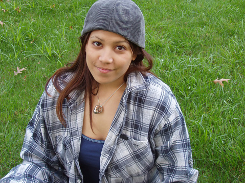 Young girl sitting in grass with backwards baseball cap and flannel shirt
