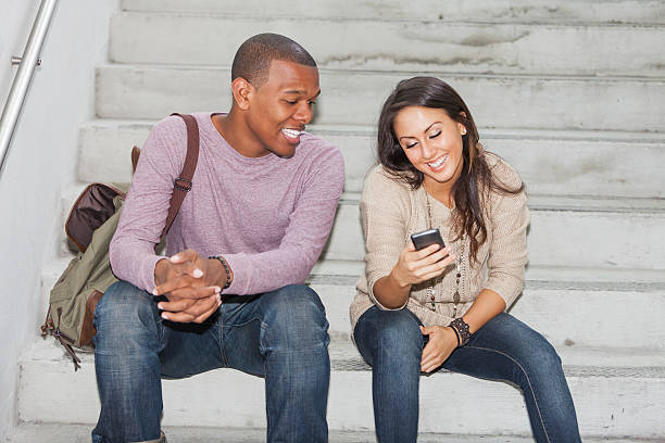 istock Young interracial couple sitting on steps with mobile phone 483784049