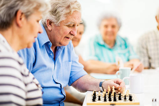 Group of people in a nursing home. Focus is on a senior man playing chess.   