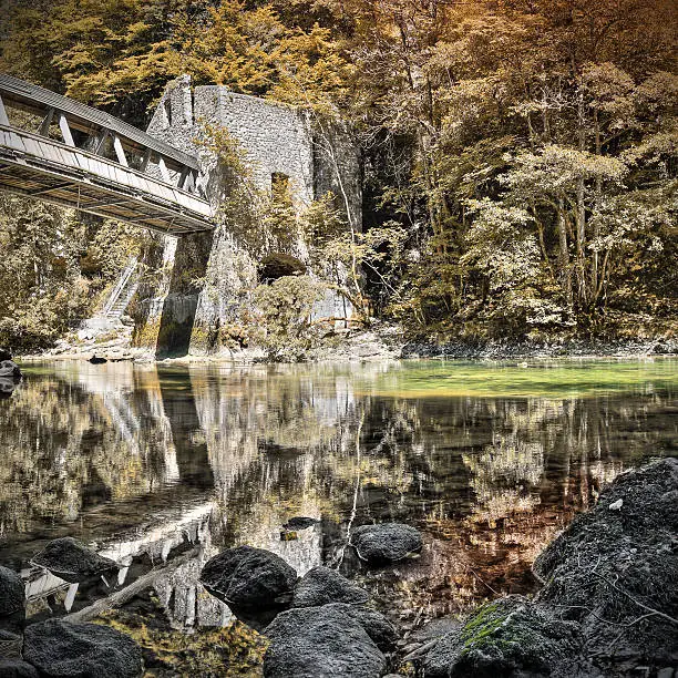Photo of Old building with bridge along river with reflection orange forest