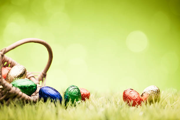 A wicker basket filled with foil-wrapped mini-Eggs in bright colours against a lightly textured green background.