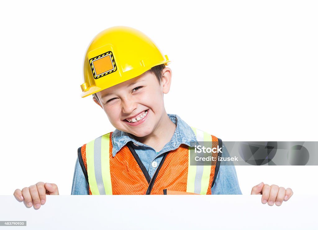 Happy Junior Construction Worker holding Whiteboard Portrait of little boy dressed as contruction worker, holding a whiteboard in hands and smiling at camera. Studio shot, isolated on white. Child Stock Photo