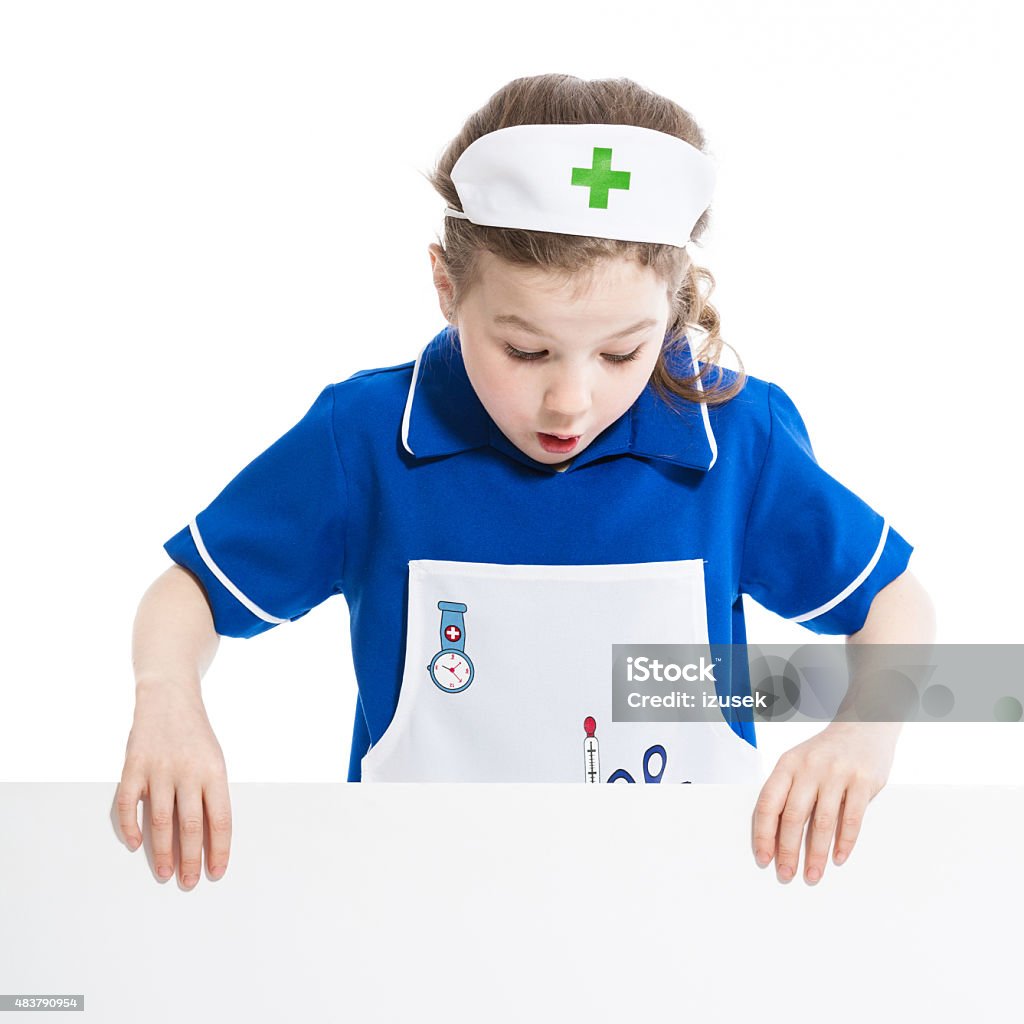 Surprised girl nurse holding a whiteboard Portrait of cute little girl dressed as a nurse holding a whiteboard in hands and looking at the board with surprised facial expression. Studio shot, isolated on white. 2015 Stock Photo
