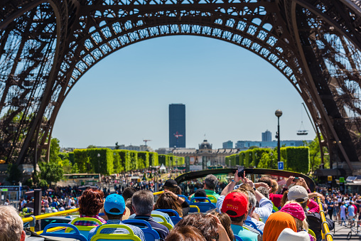 Paris, France - June 6, 2015: Tourists enjoy sightseeing tour on a hop-on-hop-off city bus in Paris on June 06, 2015. Bus is under The Eiffel tower.