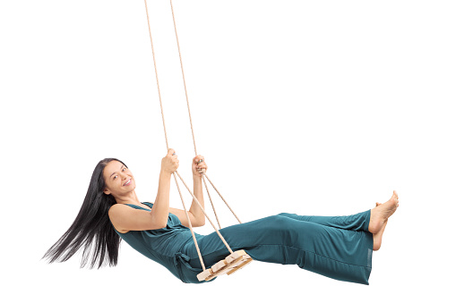Fashionable woman swinging on a wooden swing and looking at the camera isolated on white background