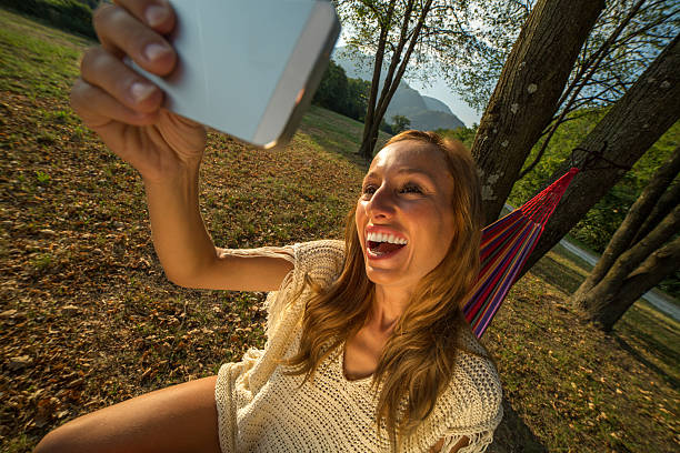 istock Young woman on hammock taking selfie using mobile phone 483802588