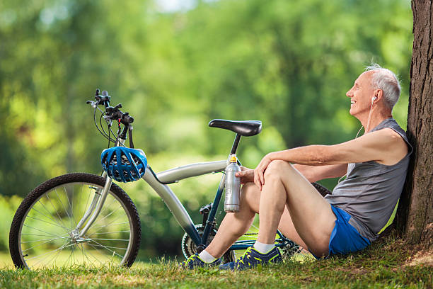 cycliste senior assis sur un arbre dans le parc - sportsman tree people recreational pursuit photos et images de collection