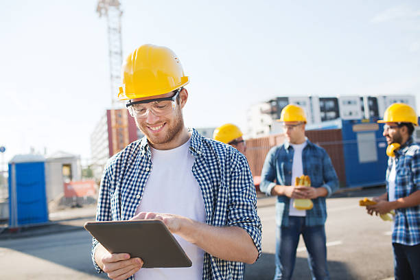 lächelnd builders in hardhats mit tablet pc - building contractor computer internet construction worker stock-fotos und bilder