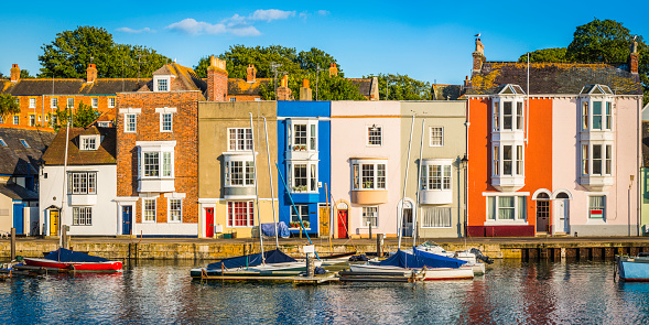 Colourful cottages and narrow higgledy-piggledy homes reflecting in the tranquil harbour of a quaint fishing port under the blue summer skies of Weymouth, Dorset, UK. ProPhoto RGB profile for maximum color fidelity and gamut.