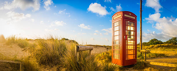 Red telephone box set amongst the golden sand dunes of a summer seaside beach illuminated by the warm sunlight of daybreak. ProPhoto RGB color profile for maximum color gamut.