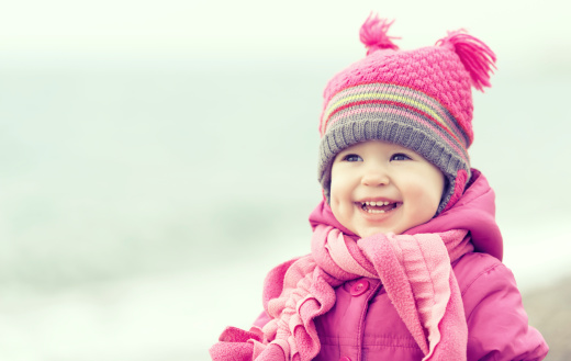Happy baby girl in a pink hat and scarf laughs