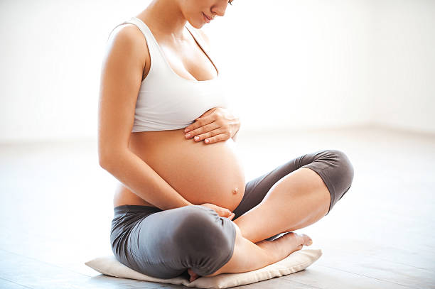 Waiting for a baby. Close-up of pregnant woman touching her belly while sitting in lotus position cross legged photos stock pictures, royalty-free photos & images