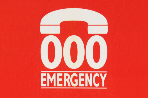 Sign indicating to call 000 in case of emergency, on the side of a phone booth in Sydney, Australia.