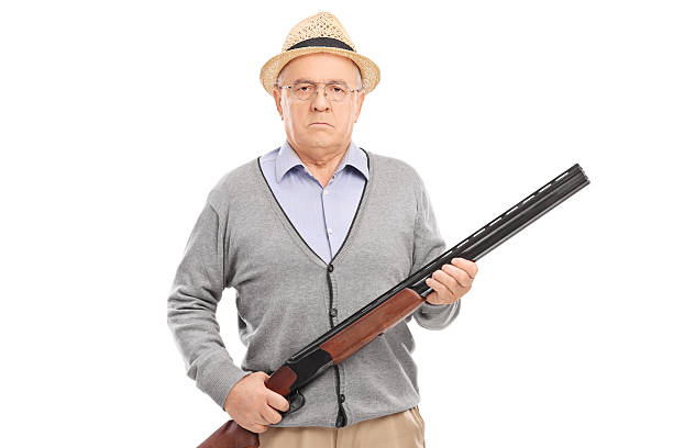 Serious senior gentleman holding a shotgun and looking at the camera isolated on white background