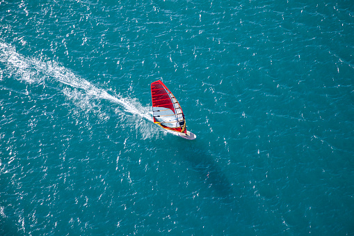 Side view of a windsurfer riding on turquoise water on a sunny day.