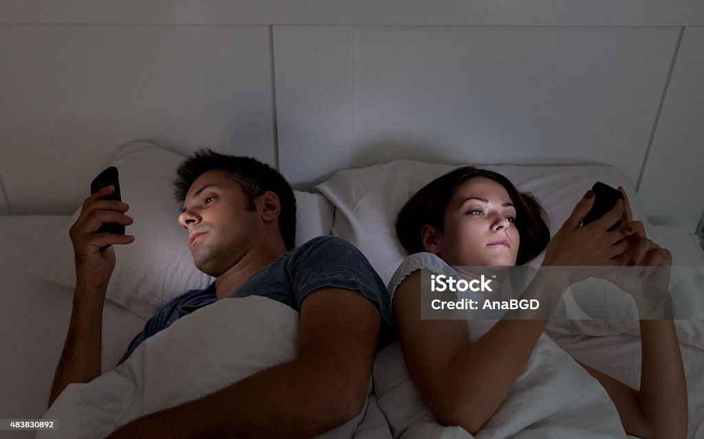 Mobile phone addiction Young couple with smartphones in their bed Couple - Relationship Stock Photo