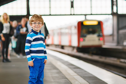 Happy little boy with glasses in a subway station. Boy looking at train. Rainy day in summer.