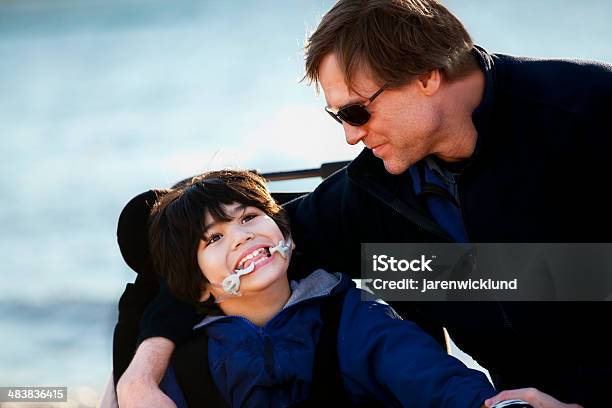 Padre Sentado Con Hijo Por Lake Shore Para Personas Con Discapacidades Foto de stock y más banco de imágenes de Niños