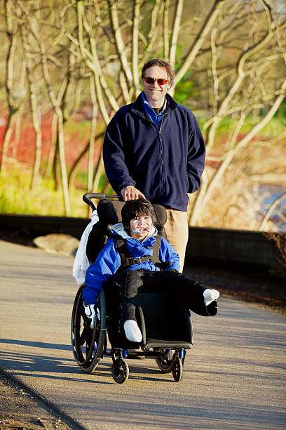istock Father walking with disabled son in wheelchair 483836431