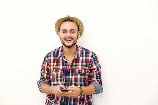 Cool young man with hat smiling with cell phone against white background