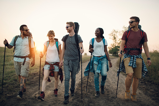 Group of young hikers, walking together. Front view of them walking with sunset in background. They enjoy sunny day. Same people you can find working in our creative office and backyard party for your coverage.