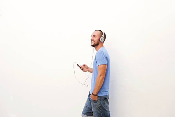 Man walking with mobile phone listening to music on headphones Happy man walking with mobile phone listening to music on headphones laughing sound men latin american and hispanic ethnicity stock pictures, royalty-free photos & images