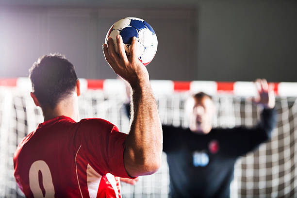 Handball player shooting at goal. Penalty shoot. Rear view of handball player shooting at goal, while goalkeeper is in the background with his hands raised.    team handball stock pictures, royalty-free photos & images