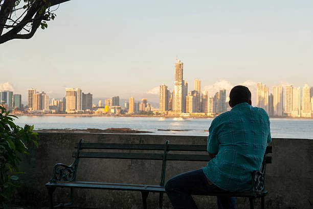 Panama City, Panama - December 21, 2008: A man sits on a bench in the historic Casco Viejo district, looking across the bay at the modern skyline of Panama City, Panama