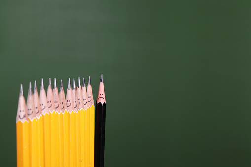 A black pencil with a sad face at the end of a line.  All other pencils are yellow.