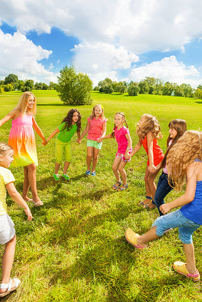 Large group of happy girls play roundelay and stand in circle in the park on the green grass on sunny summer day