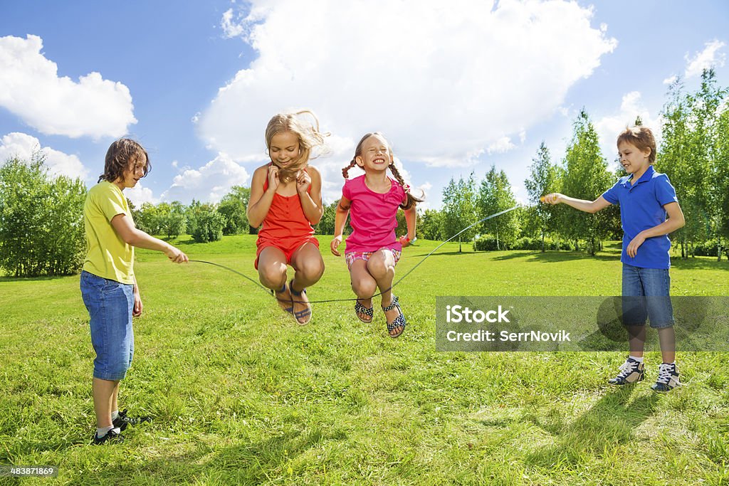 Girls jumping over the rope with friends Two girls jumping over the rope with boys rotating the rope Jumping Rope Stock Photo