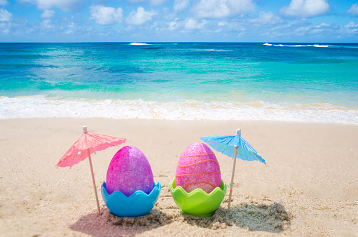 Two easter eggs with cocktail umbrella on the sandy beach