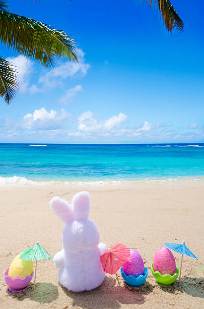 Easter bunny and color eggs with cocktail umbrellas on the sandy beach by the ocean