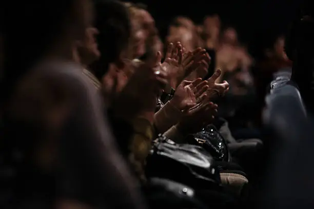 View down a row of people sitting in an audience of people clapping their hands in appreciation of a performance