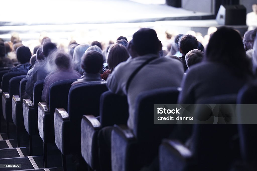 Audience sitting in tiered seating Audience sitting in tiered seating watching a live performance or cinema, view from behind Movie Theater Stock Photo