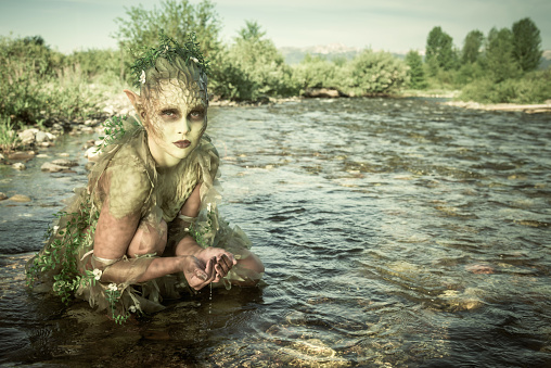 Water Nymph crouching in a river with clear water running through her hands. The Naiads or Potamides are a type of Water Nymphs of Greco-Roman Mythology.