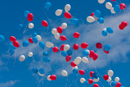 A lot of red white and blue balloons fly in the sky