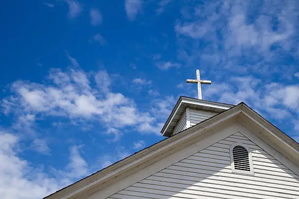 Wooden cross on a simple steeple set against a sunny summer blue sky.