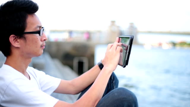 Man reading on his tablet at riverside