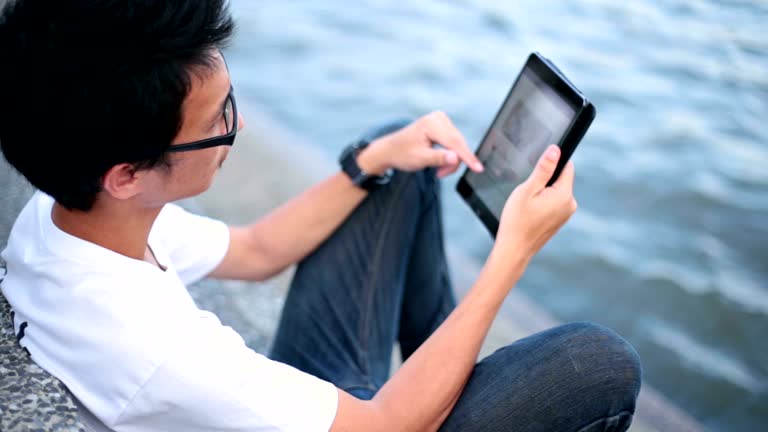 Man reading on his tablet at riverside