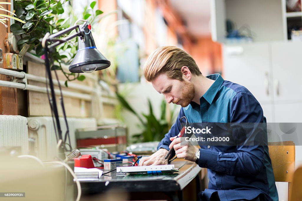 Young handsome man soldering a circuit board Young handsome man soldering a circuit board and working on fixing hardware Road Sign Stock Photo