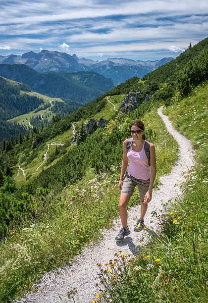Beautiful woman in a sports outfit hiking. Woman hiking up the Jenner from the Koenigssee in Berchtesgaden. You can see the famous Watzmann Mountain in back. Nikon D810. Converted from RAW.