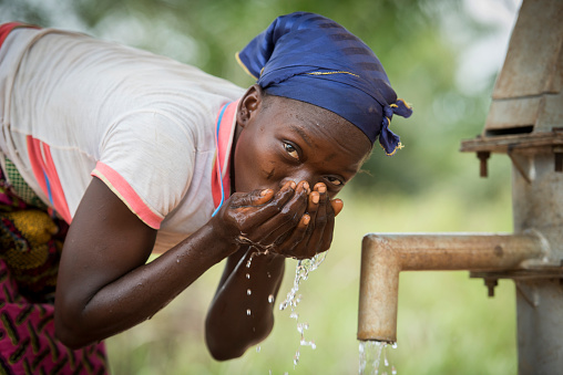 Village de Guede Codji, Benin, March 11, 2015: Woman is drinking water from a pump. This well provides clean water for the whole village.